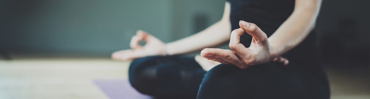 Mulher vestida de preto fazendo meditação em tapete: pernas cruzadas em posição de lótus
