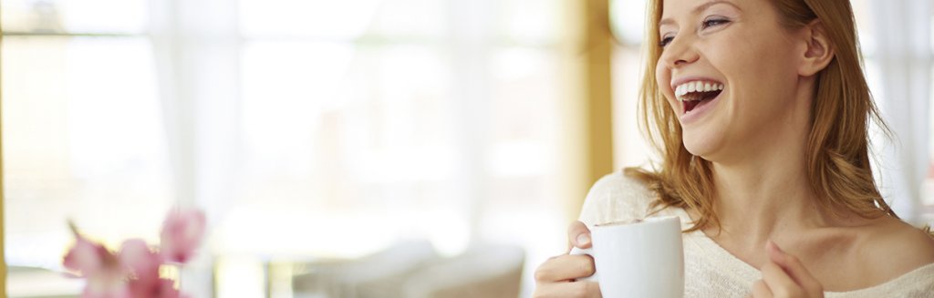 Mulher sorrindo feliz com uma xícara de café na mão: alegria e vida leve