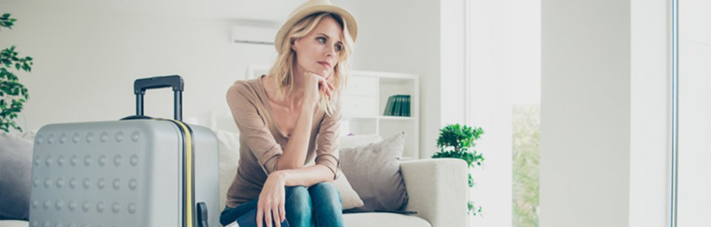Mulher sentada em um sofá com uma mala ao lado aparentando desconforto