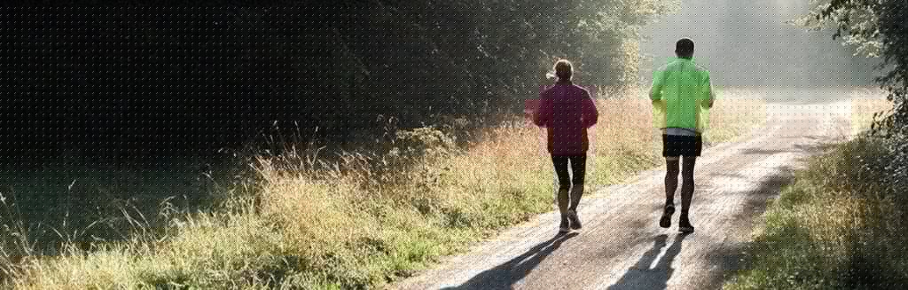 Duas pessoas praticando caminhada ou corrida em um lugar com áreas verdes ao redor