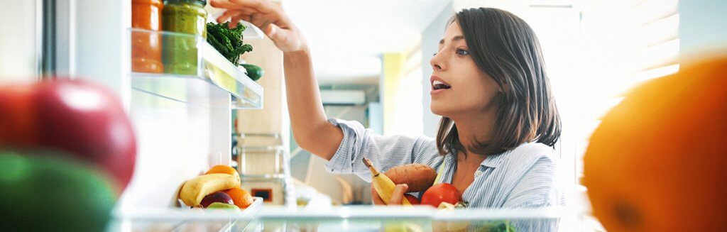 Mulher olhando a geladeira com alimentos saudáveis armazenados