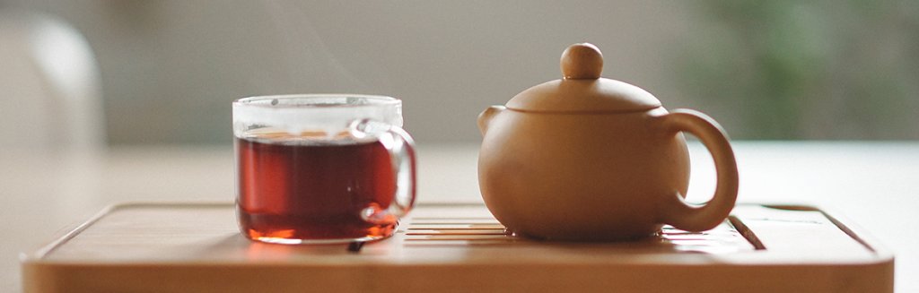 Xícara de chá ao lado de chaleira em uma superfície de madeira