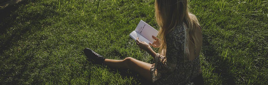 Mulher loira sentada na grama lendo um livro: leitura ao ar livre na ntureza 