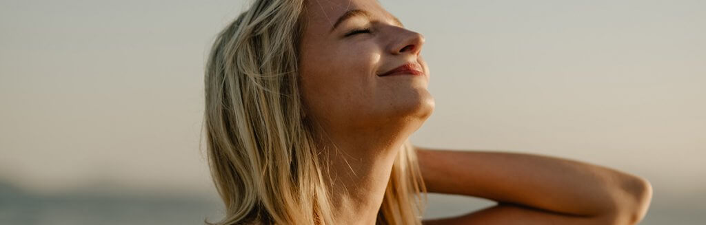 Mulher loira de olhos fechados e sorrindo com expressão satisfeita