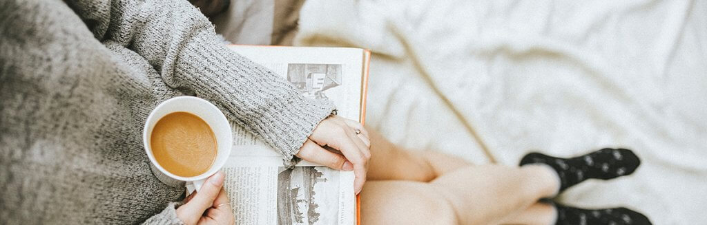 Pessoa sentada confortável lendo um livro com uma xícara de café na mão