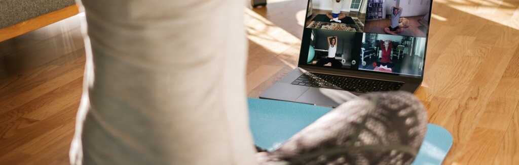 Pessoa em um tapete praticando exercícios em videochamada com outras pessoas fazendo o mesmo