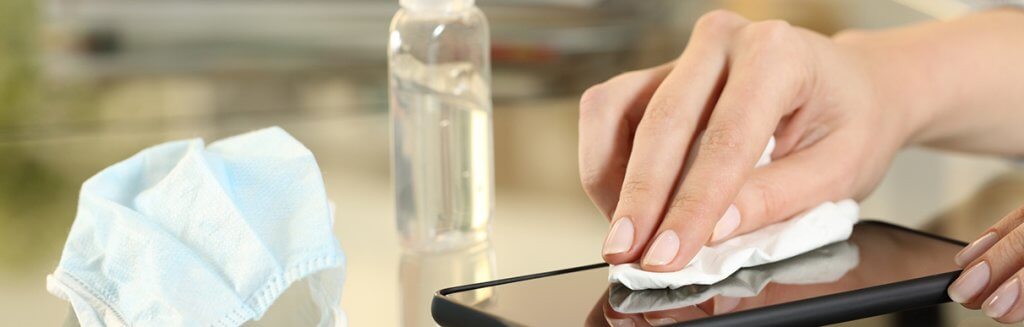 Pessoa higienizando um celular com uma máscara ao lado