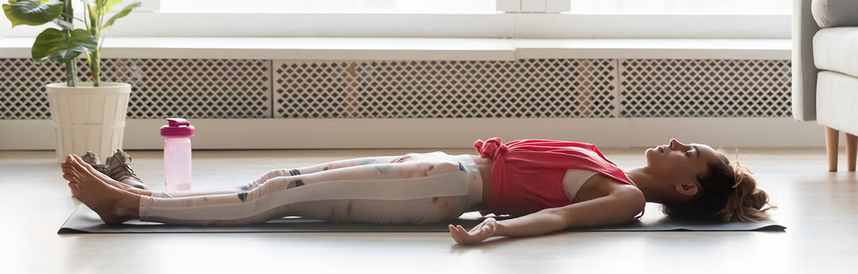 Mulher deitada em tapete no chão fazendo exercícios de respiração