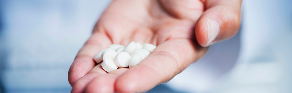 Mão de uma pessoa segurando pílulas de um remédio
