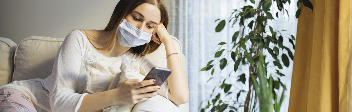 Mulher de máscara sentada no sofá segurando o celular