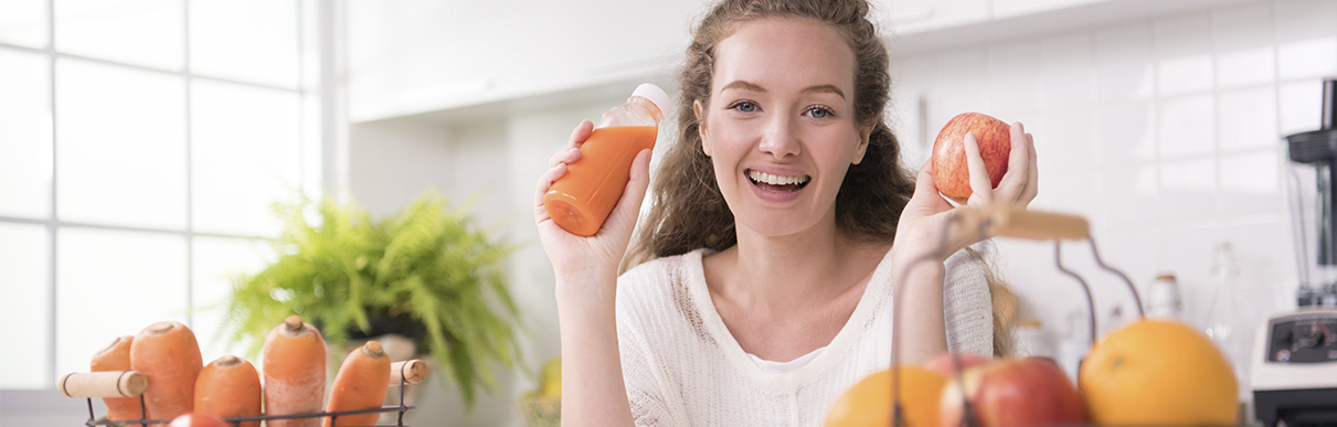 Mulher sorrindo com uma garrafa de suco em uma mão e uma maçã em outra