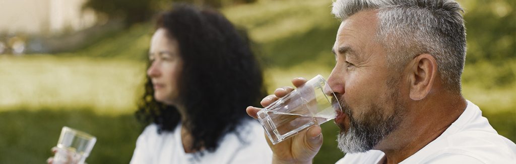 Homem idoso e mulher mais jovem do que ele sentados na grama bebendo água: hidratação