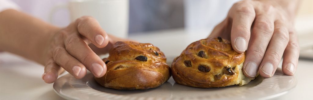 Prato com 2 brioches com gotas de chocolate com uma pessoa com as mãos neles: pão doce