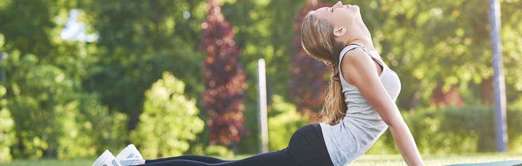 Mulher jovem fazendo posição de yoga (pose da serpente) em um parque ou área verde