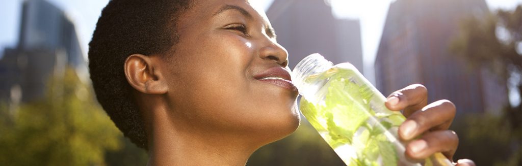 Mulher negra feliz tomando bebida saudável ao ar livre