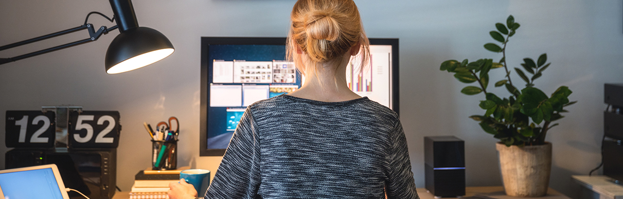 Mulher sentada em frente ao computador ao lado de uma luminária simbolizando o trabalho