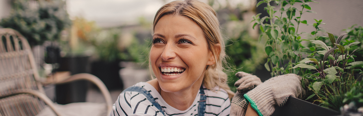 Mulher loira feliz cuidando das verduras de sua horta em casa: vida saudável