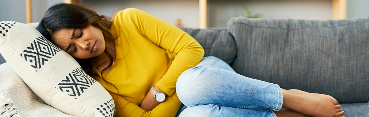 Mulher deitada em um sofá com as mãos na barriga simbolizando dor