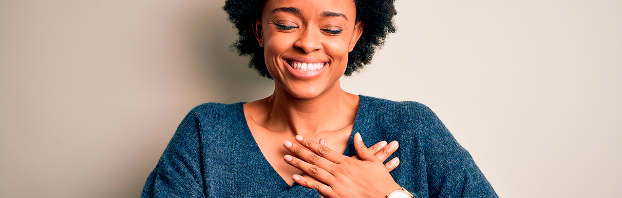 Mulher sorrindo de olhos fechados com a mão no peito