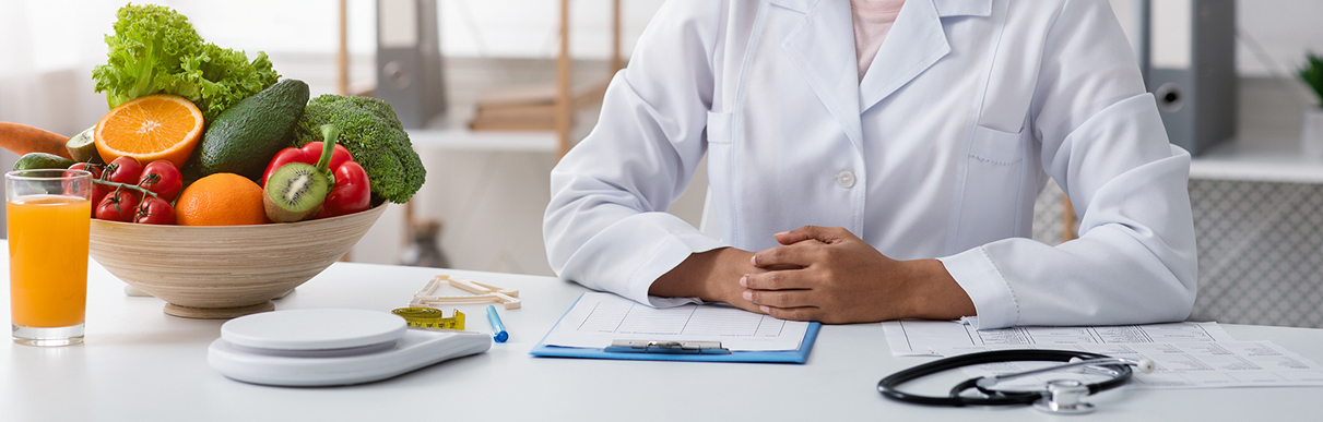 Mulher de jaleco ao lado de várias verduras e frutas saudáveis