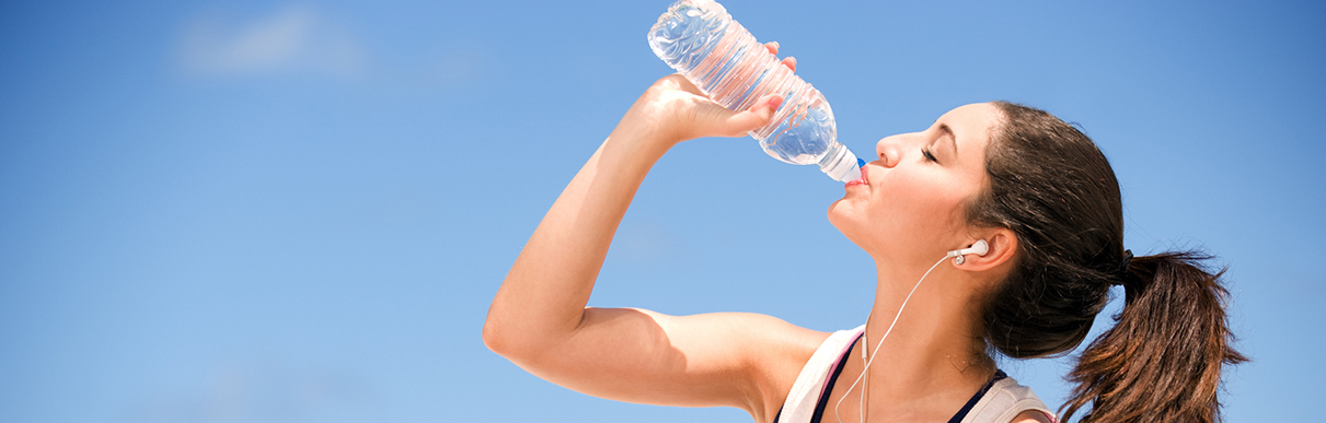 Mulher com fones de ouvido bebendo água de uma garrafa
