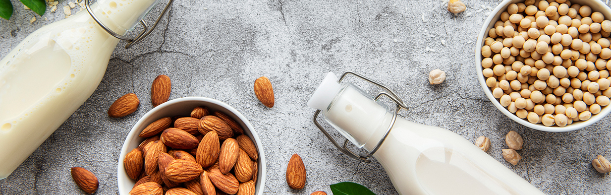 Garrafas de leite ao lado de amêndoas e soja, representando leites de amêndoas e leite de soja
