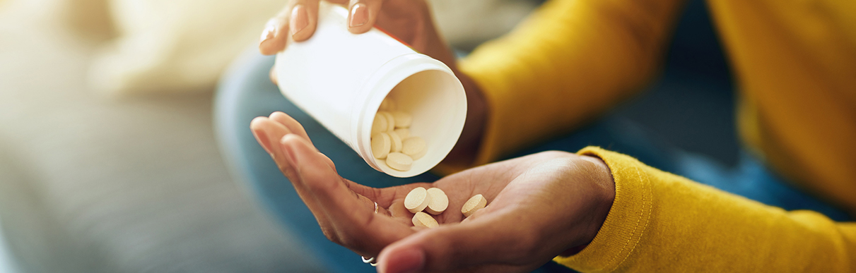 Pessoa pegando comprimidos com uma das suas mãos