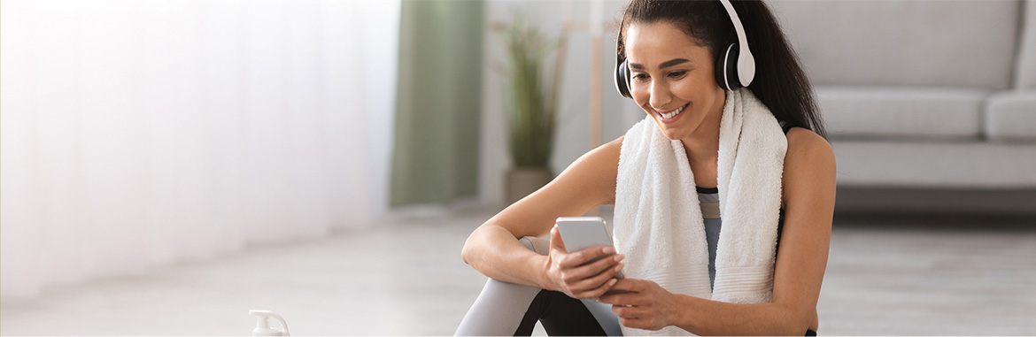 Mulher sorrindo de fone de ouvido escolhendo uma música antes de se exercitar